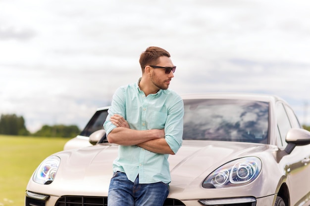 road trip, transport, leisure and people concept - man in sunglasses standing at car outdoors
