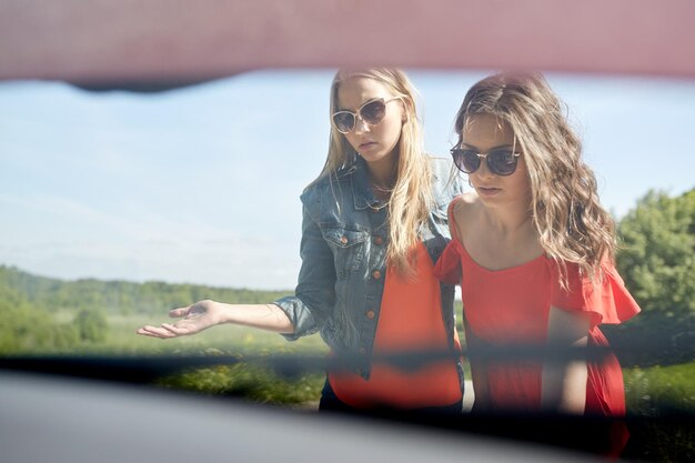 road trip, transport, reizen en mensen concept - jonge vrouwen met open motorkap van kapotte auto op het platteland