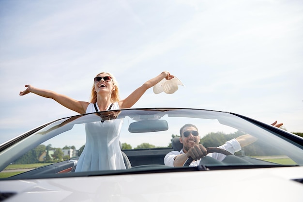 road trip, travel, dating, couple and people concept - happy man and woman driving in cabriolet car outdoors