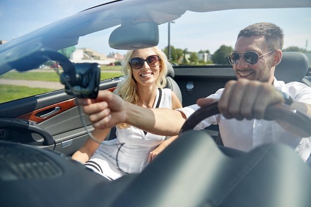 road trip, travel, summer vacation, technology and people concept - happy man and woman driving car and using gps navigator in cabriolet car