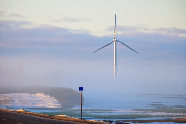 Road to wind power stations, half hidden ones in the fog early during the sunrise in the winter. Renewable energy concept.