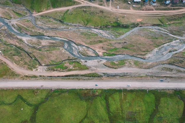 A road with a green field and a road that has a small river running through it.