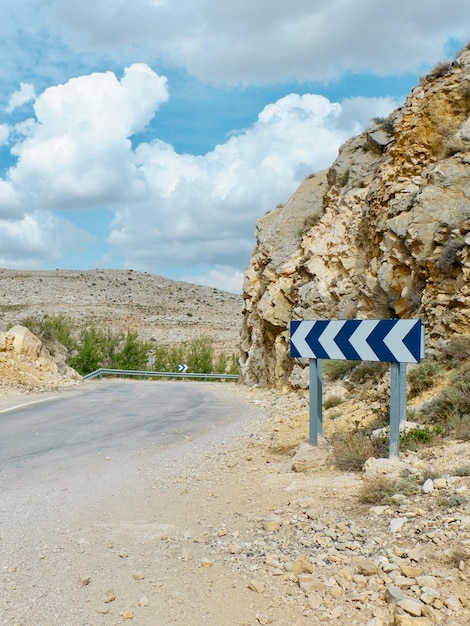 Road with a rocky turn and direction sign with vivid cloudscape\
over it conceptual for career future change