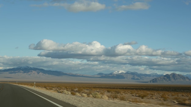 Roadtrip, autorijden van death valley naar las vegas, nevada, vs. liftend op reis in amerika. snelwegreis, dramatische sfeer, wolken, bergen en mojave-woestijnwildernis. uitzicht vanuit auto