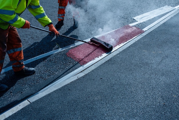 Roadworker che applica segnaletica stradale termoplastica sull'asfalto appena posato durante la nuova rotatoria e la costruzione di strade