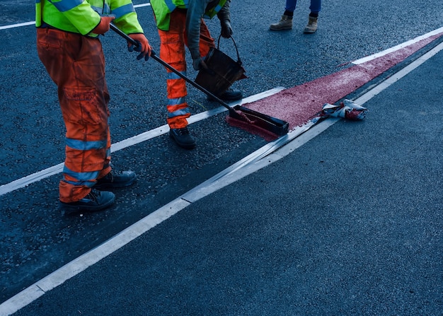 Roadworker applying thermoplastic road marking on the freshly laid tarmac during new roundabout and access road construction