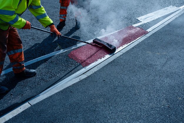 新しいラウンドアバウトと道路建設中に、敷設されたばかりの舗装道路に熱可塑性道路標示を適用するロードワーカー