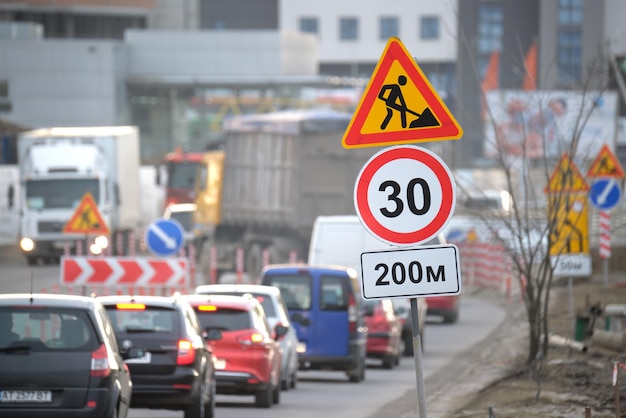 Roadworks warning traffic signs of construction work on city\
street and slowly moving cars