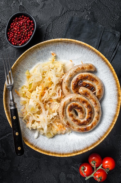 Roast bavarian spiral meat sausages on a plate with sauerkraut Black background Top view