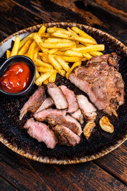 Roast BBQ pork chop steak on plate with potato chips Wooden background Top view