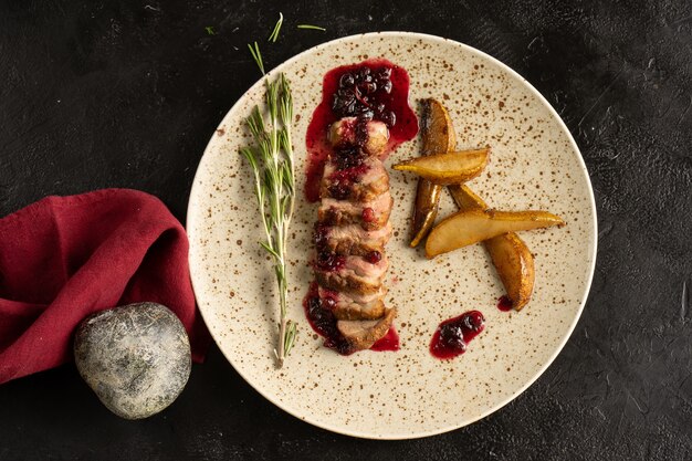 Roast beef with cranberry sauce, rosemary and fried pear. Plate with meat dish on a black table. Top view.