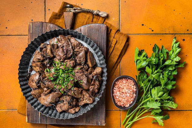 Roast chicken liver with onions and herb in a steel plate Orange background Top view