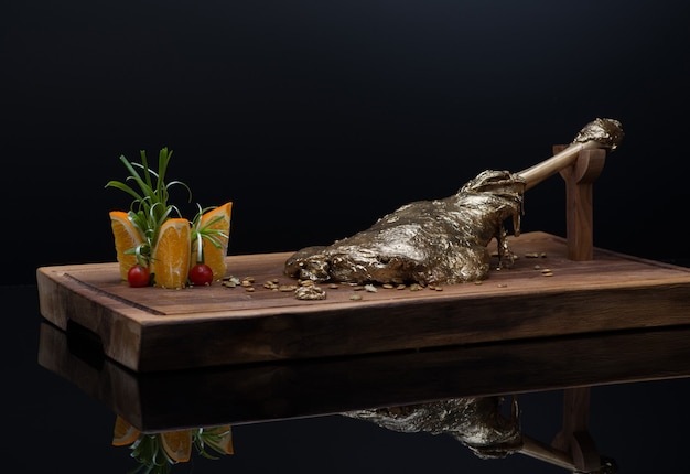 Roast meat with bone in gold leaf on a wooden tray