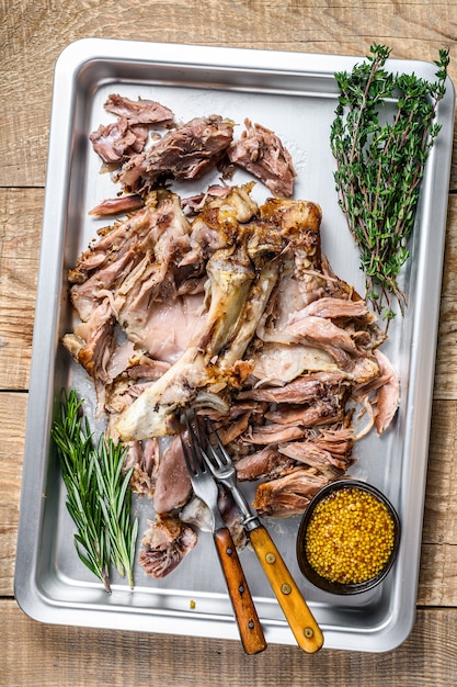 Roast pork knuckle eisbein meat on a baking pan with herbs. Wooden background. Top view.