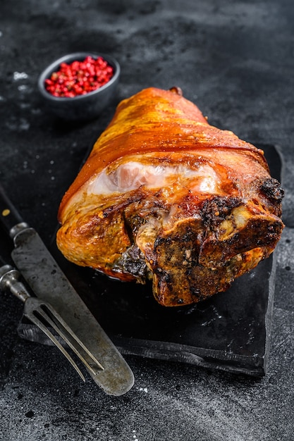 Roast pork knuckle with pink pepper and spices. Black background. Top view.