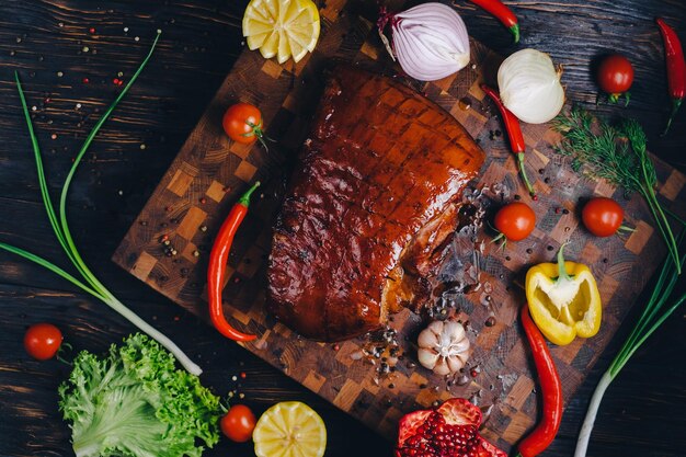 roast pork in a smokehouse standing on a cutting board garnished with rosemary pepper chili pepper tomato lemon pomegranate aromatic baked meat