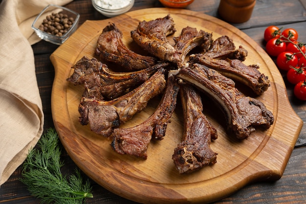 Roast rack of lamb served on wooden board on dark wooden