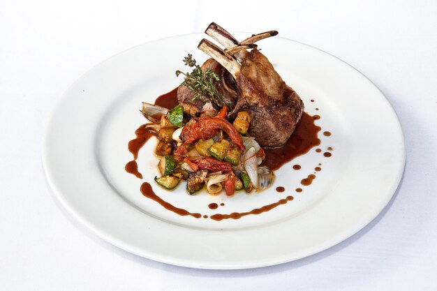 Roast rack of lamb or veal accompanied with vegetables and sauce white background food gastronomy