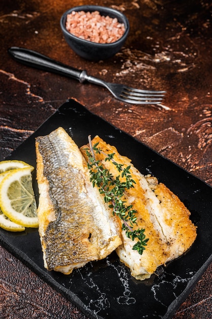 Roast sea bass fillet with lemon and thyme seabass fish Dark background Top view