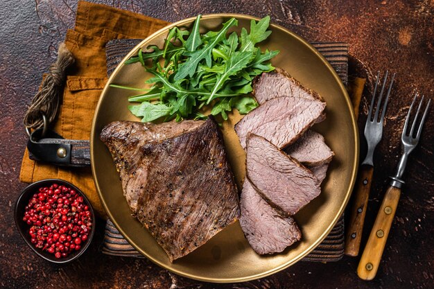 Bistecca di manzo arrosto tri tip o controfiletto su un piatto con rucola sfondo scuro vista dall'alto