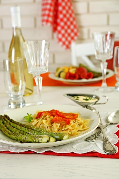 Roasted asparagus and tasty pasta with vegetables on plate on wooden table background