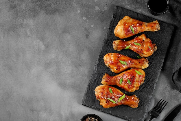 Roasted Baked chicken legs drumsticks on black slate board on dark background Copy space for text