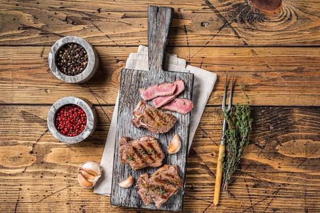 Bistecche di lombo di agnello arrostite nel barbecue, cotolette su una tavola di legno con erbe aromatiche. fondo in legno. vista dall'alto.