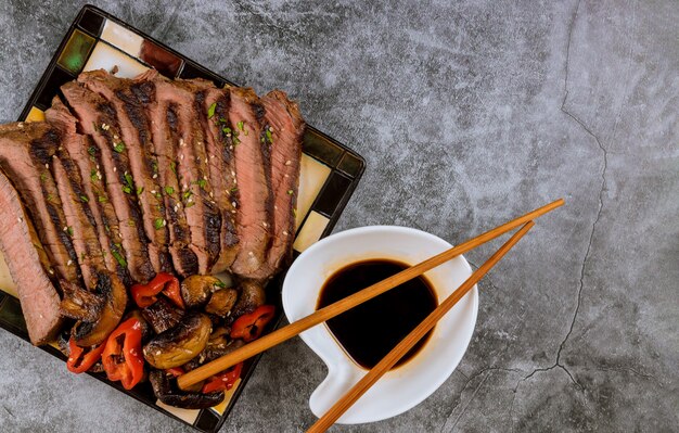 Roasted beef with soy sauce on plate, top view.