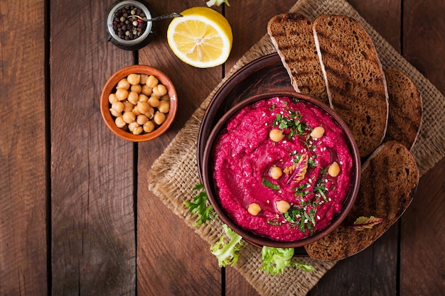 Hummus di barbabietole arrosto con pane tostato in una ciotola di ceramica su uno sfondo scuro