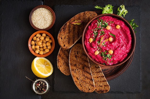 Roasted Beet Hummus with toast in a ceramic bowl on a dark background