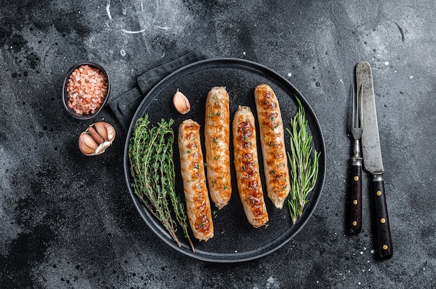 Roasted Bockwurst pork meat sausages in a plate. Black background. Top view.