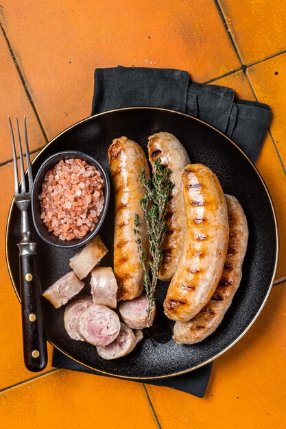 roasted bratwurst and bockwurst pork meat sausages in a plate orange background top view