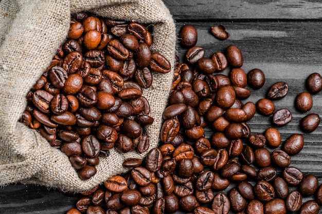 Photo roasted brown coffee beans falling out from the burlap bag on the table fresh natural grains over the gray background closeup