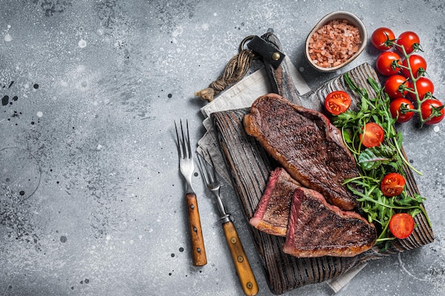 Roasted cap rump or Top sirloin beef meat steak on wooden board with salad. Gray background. Top view. Copy space.