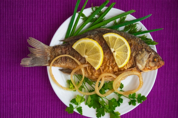 Roasted carp fish with greens on a white plate. The top view