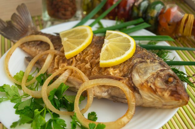 Roasted carp fish with greens on a white plate.