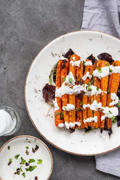 Roasted carrot sticks on a white plate Baked carrots with herbs and spices on gray background