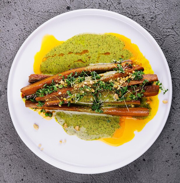 Roasted carrots are served on a white stoneware plate alongside a pesto