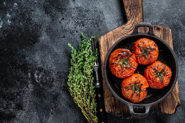 Roasted cherry tomatoes with thyme in a pan. Black background. Top view. Copy space.