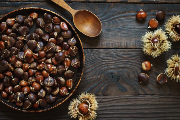 Roasted chestnuts in a pan and whole fruits on a wooden table