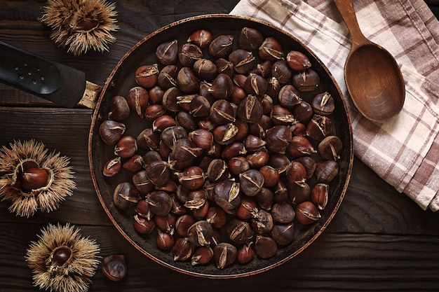 Foto castagne arrostite in padella e frutti interi su un tavolo di legno