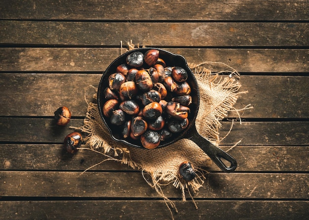 Roasted chestnuts in a small iron pan on a aged brown wooden table