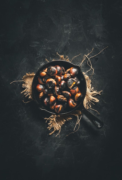 Roasted chestnuts in a small iron pan on a dark table