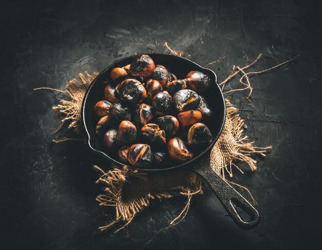 Roasted chestnuts in a small iron pan on a dark table