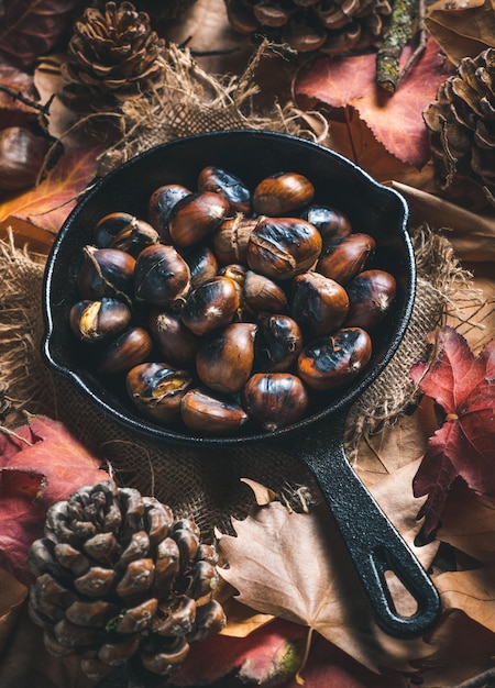 Roasted chestnuts in a small iron pan on a table with autumn leaves and pine cones