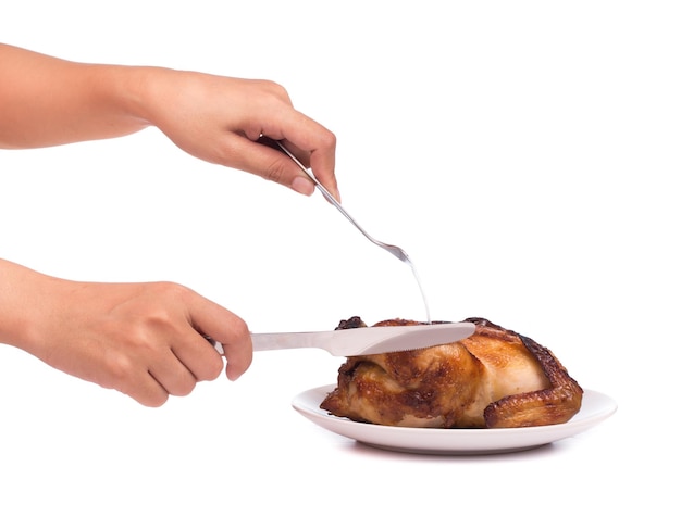 Roasted chicken being cut by knife and fork on a dish isolated on white background