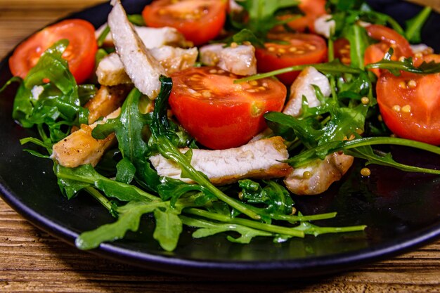 Roasted chicken breasts and salad with arugula and cherry tomatoes in a black plate