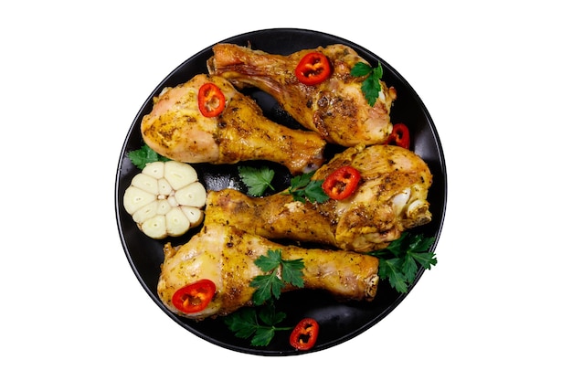 Roasted chicken drumsticks with spices in a black plate isolated on white background Top view