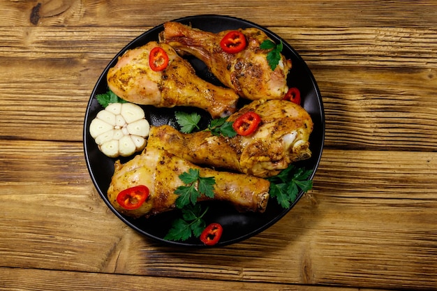 Roasted chicken drumsticks with spices in a black plate on a wooden table Top view