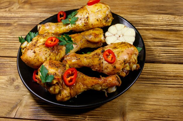 Roasted chicken drumsticks with spices in a black plate on a wooden table